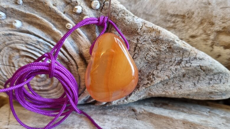 Karneola kulons "Enerģijas pieplūdums" nr 4. Izmērs 2.5 x 2 cm Ar lillā auklu