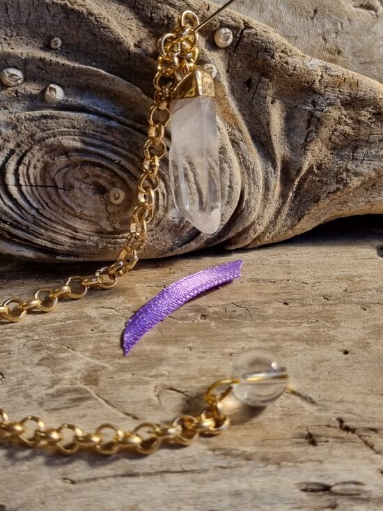 Kalnu kristāla svārstiņš "Enerģijas deva" nr 1. Izmērs 3 x 1 cm Lillā bantīte Ar dabīgiem iespiedumiem