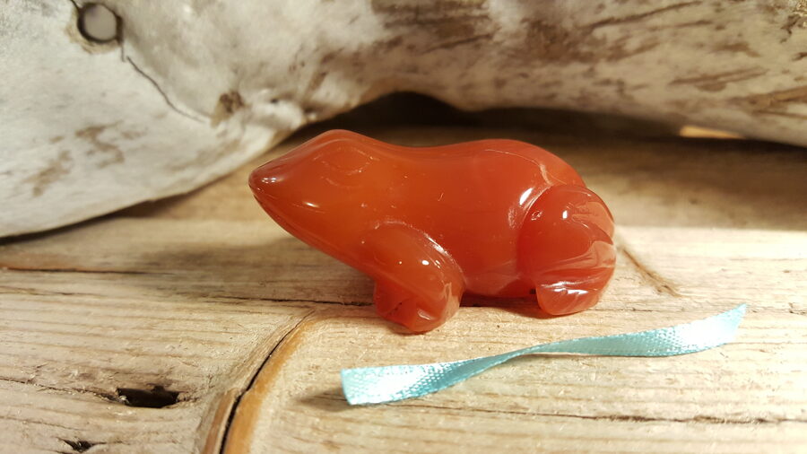 Karneola varde "Dzīvesprieks" nr 2. Izmērs 5 x 2.8 x 2 cm  Simbolizē jaunu dzīves sākumu izturību un spēku  Zila bantīte