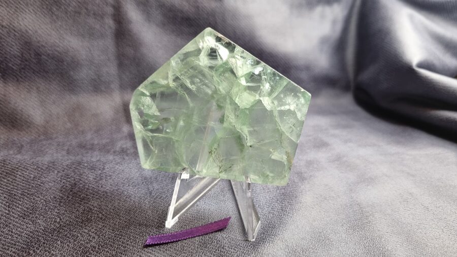  Fluorīta plāksne "Zaļā pasaka"  Izmērs 7.3 x 6 x 1 cm Dzīvojamā istabā uz galda Ar statīvu Ar dabīgām plaisām Lillā bantīte