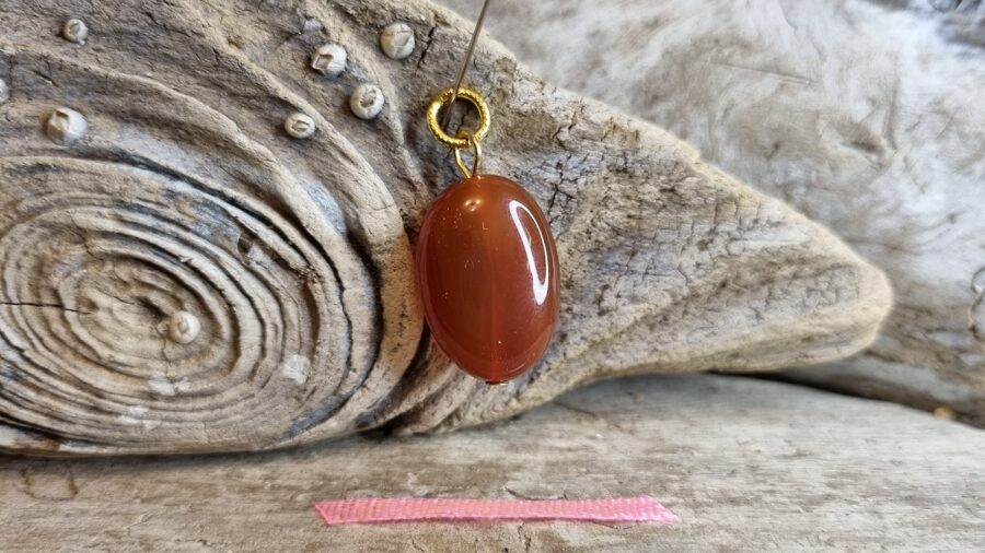 Liels karneola kulons "Aizsargamulets" nr 2. Izmērs 2 x 1.5 cm Rozā bantīte Zelta krāsas metāls